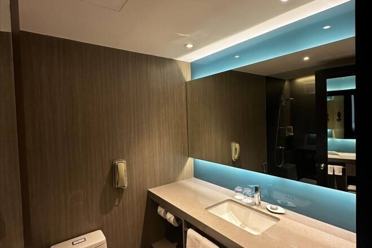 A modern bathroom with a wooden wall, a large mirror, a sink, and a shower area.
