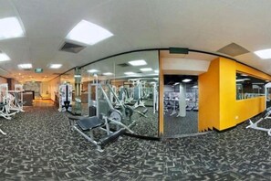 Un gimnasio con equipo de ejercicio, un espejo grande y piso alfombrado.