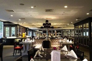Un interior de restaurante con mesas dispuestas para comer, una zona de bar y una araña.