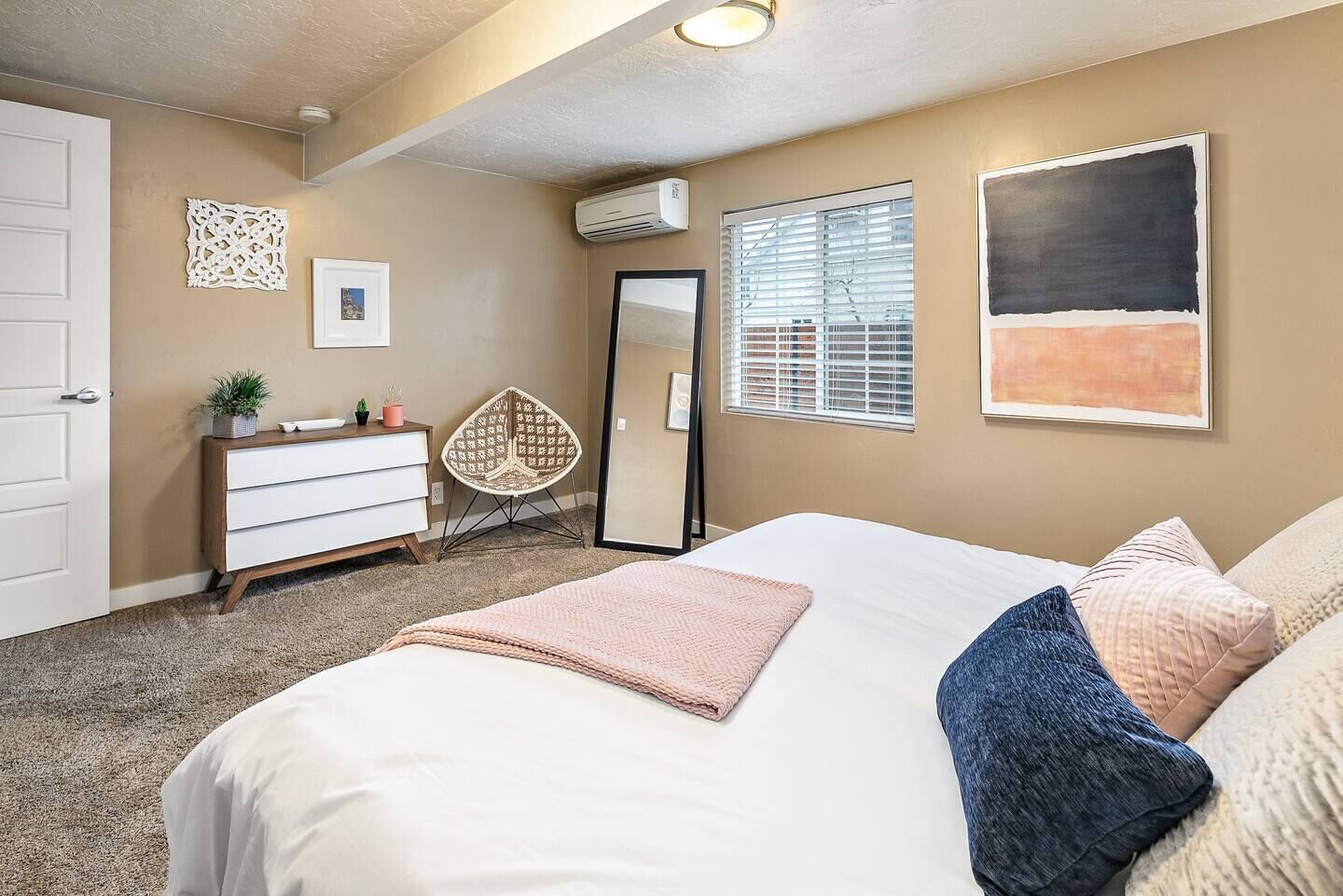 A bedroom with a large bed, a dresser, a chair, a mirror, and artwork on the walls.
