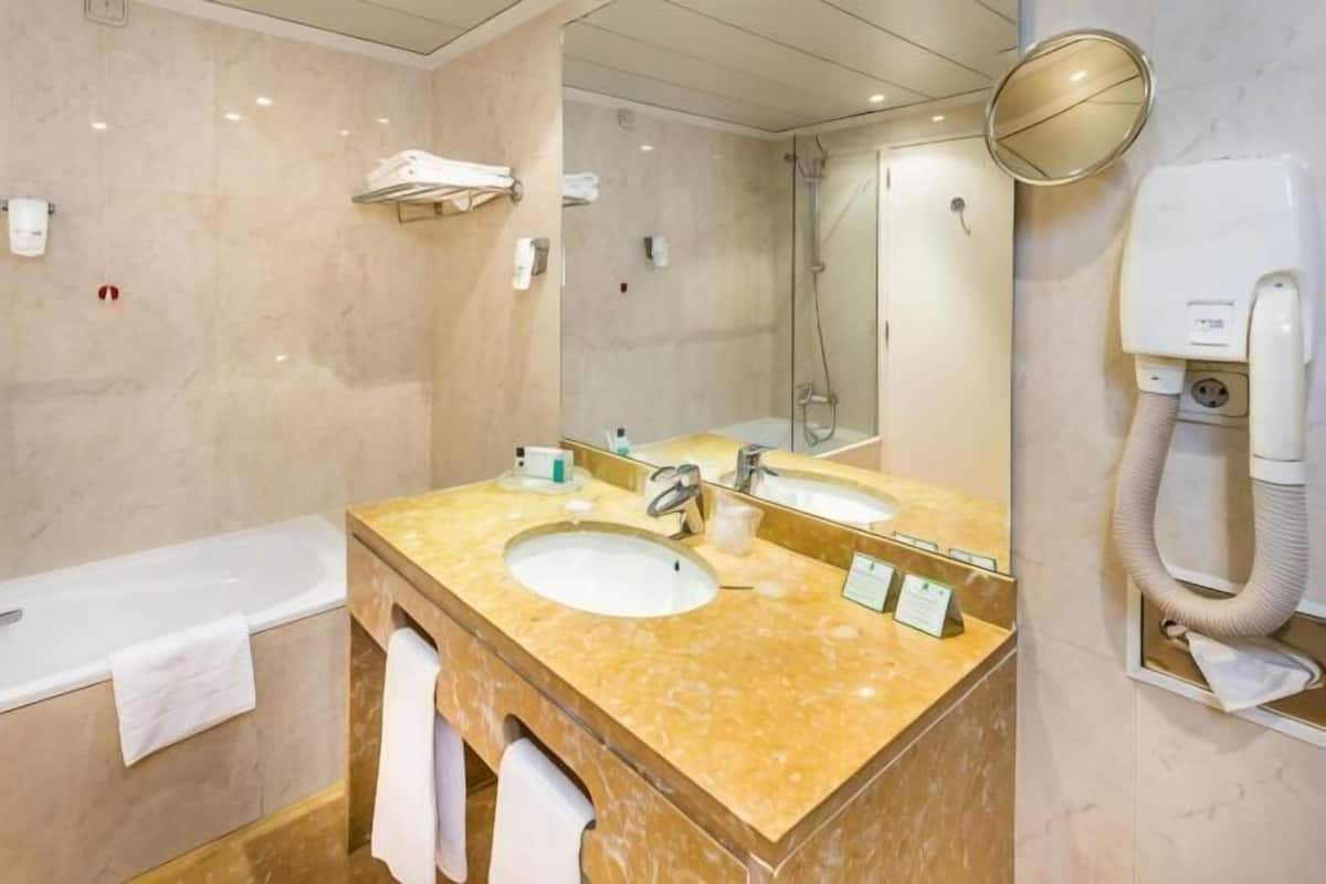 A bathroom with two sinks, a bathtub, a mirror, a towel rack, and a hairdryer.