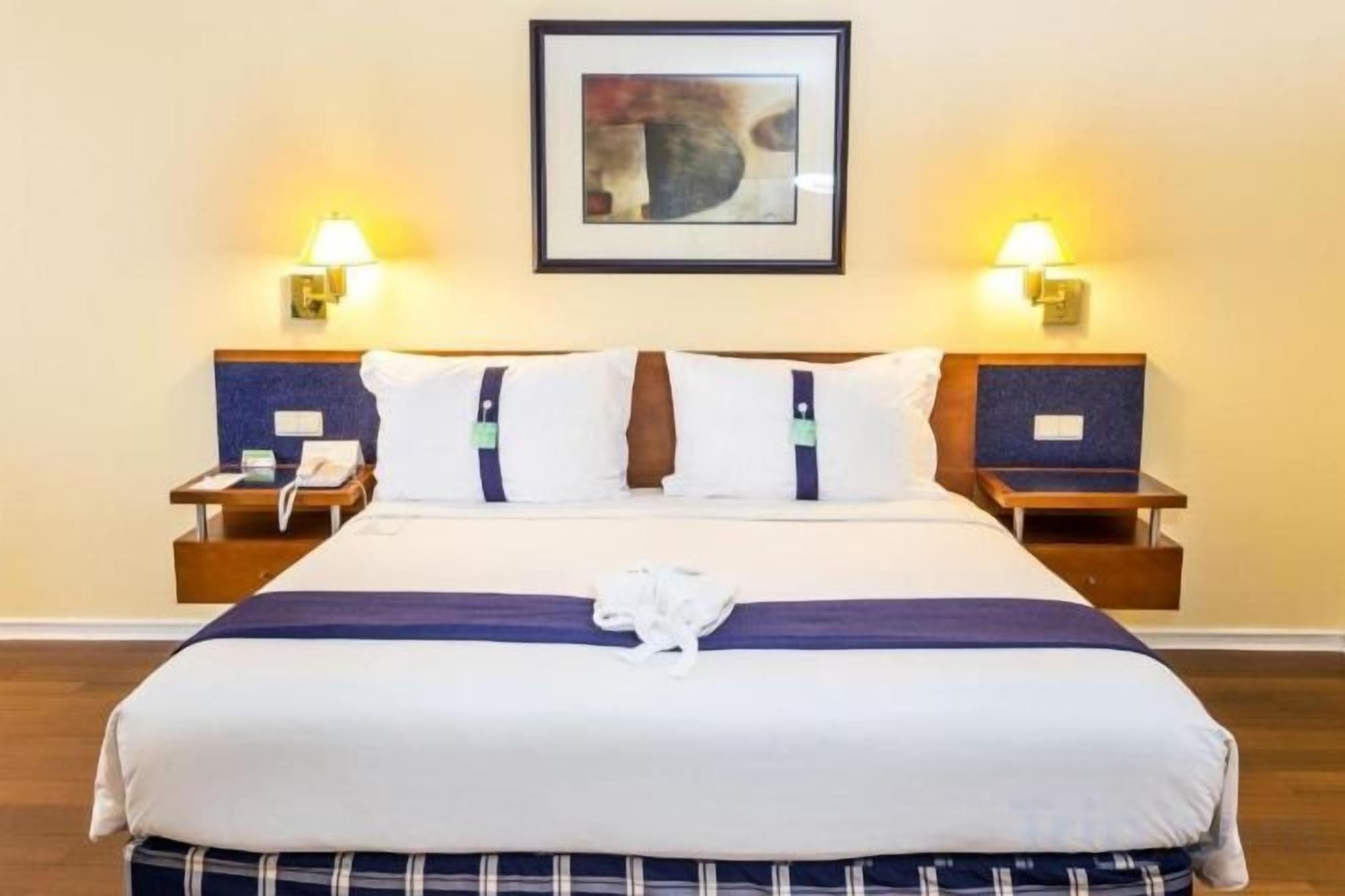 Una camera d'albergo con un letto grande, due comodini, un quadro incorniciato appeso al muro e due lampade a parete.