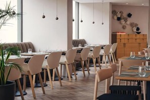 A modern dining area with round tables, chairs, and hanging pendant lights. - Holiday Inn LISBON by IHG (Lisbon)
