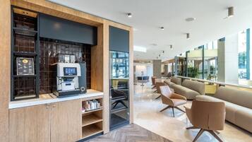 Un intérieur moderne avec une machine à café, un coin salon et de grandes fenêtres.
