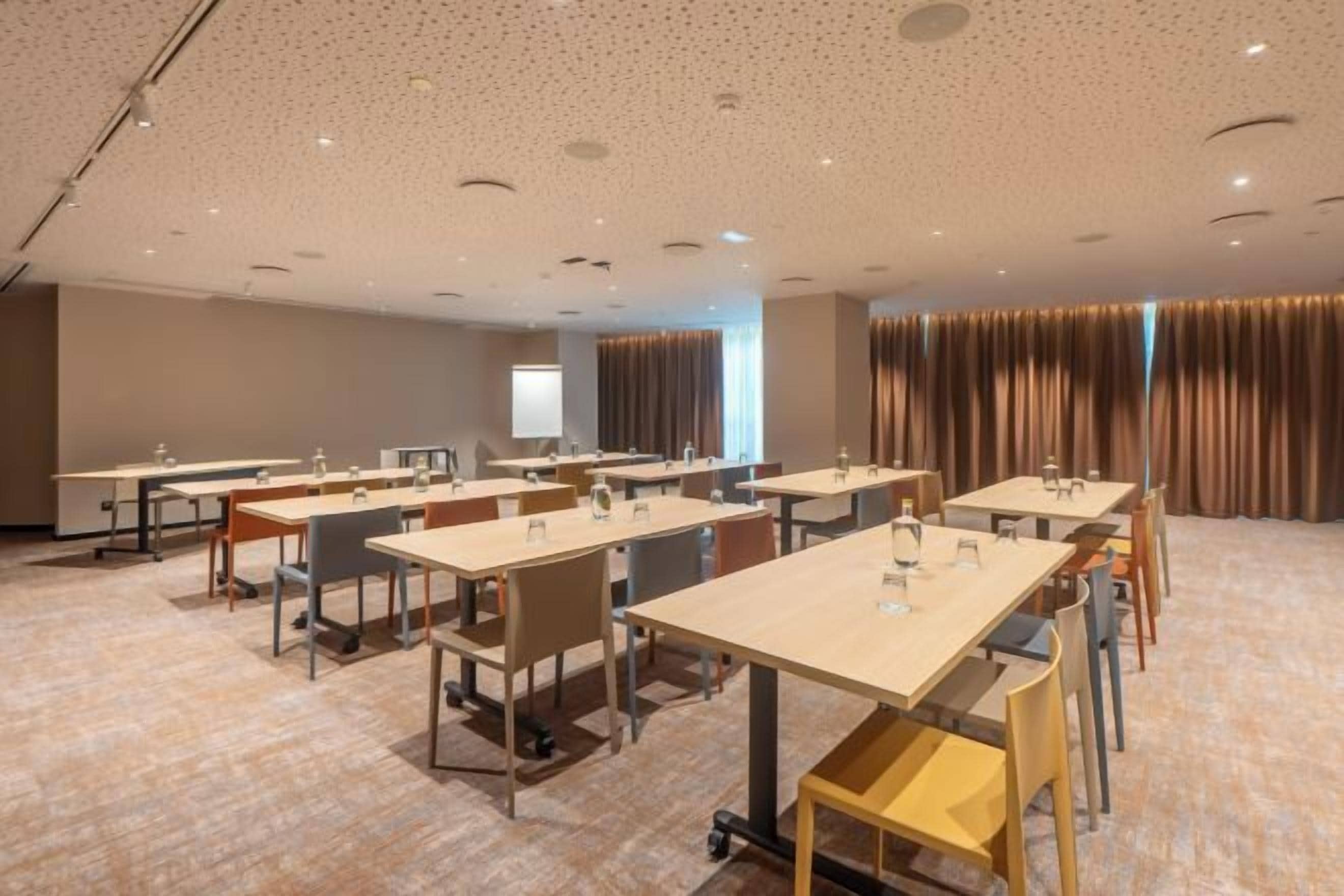A conference room with multiple tables and chairs, a projector screen, and a large window with curtains.