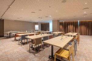 A conference room with multiple tables and chairs, a projector screen, and a large window with curtains.