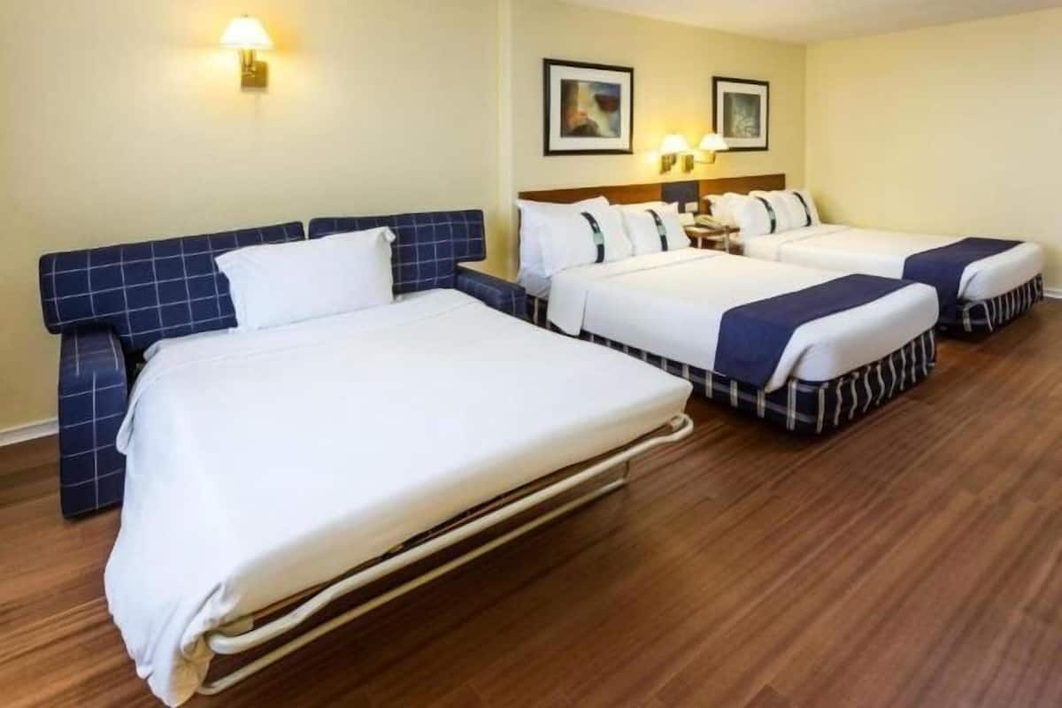A hotel room with two beds, a wooden floor, and wall-mounted lamps.