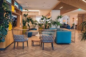 Um hall moderno com assentos, plantas e piso de madeira.