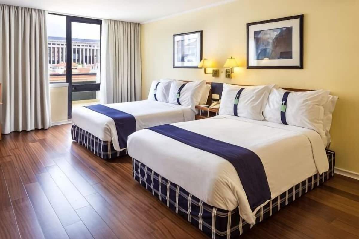 A hotel room with two beds, a balcony, and a city view.