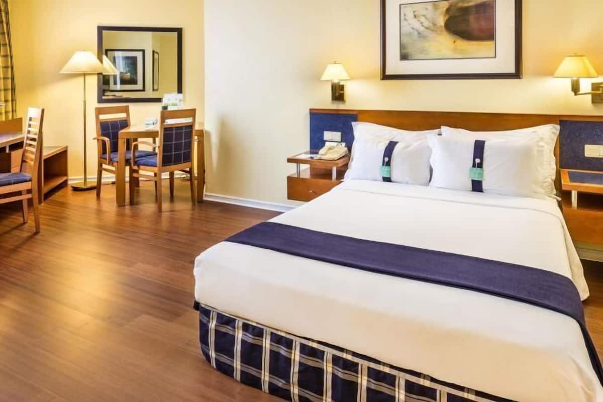 A hotel room with a large bed, a desk with a chair, a nightstand, and two wall-mounted lamps.