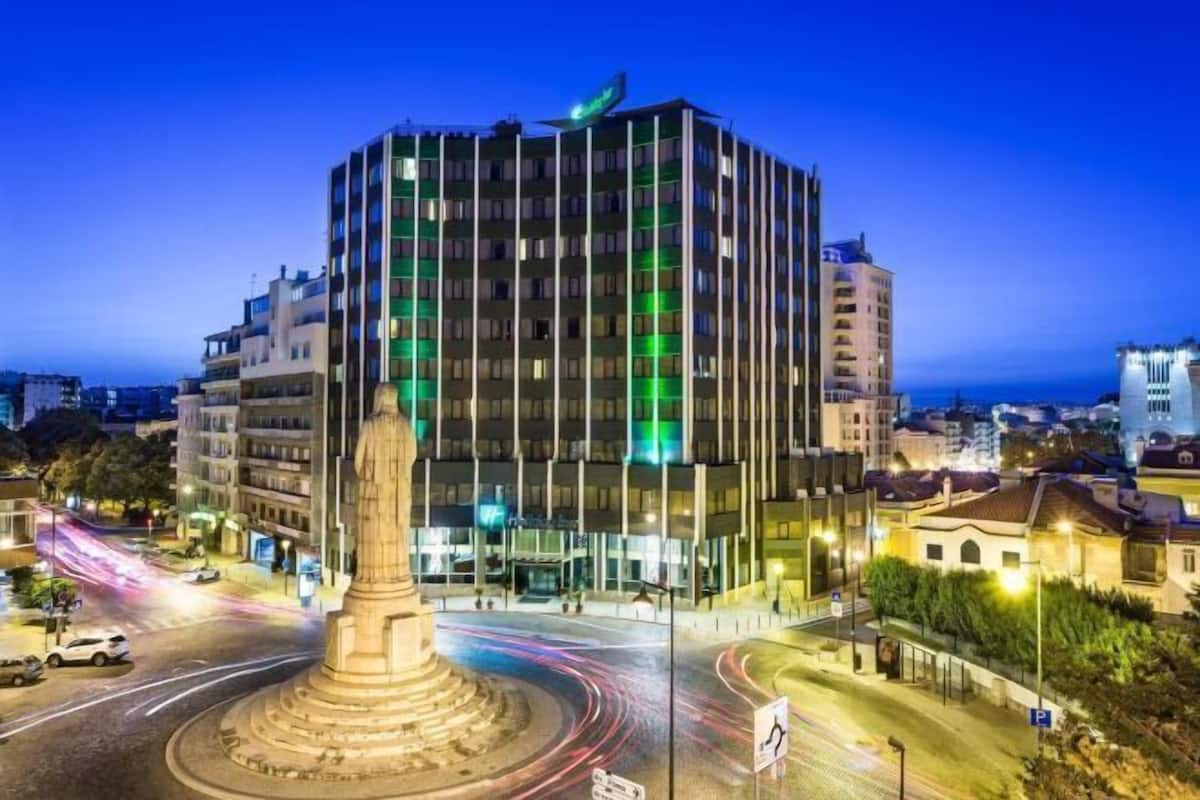 A modern hotel with a central courtyard, a roundabout, and a view of the sea.