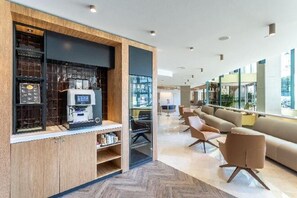A modern hotel lobby with a coffee machine, seating area, and large windows. - Holiday Inn LISBON by IHG (Lisbon)