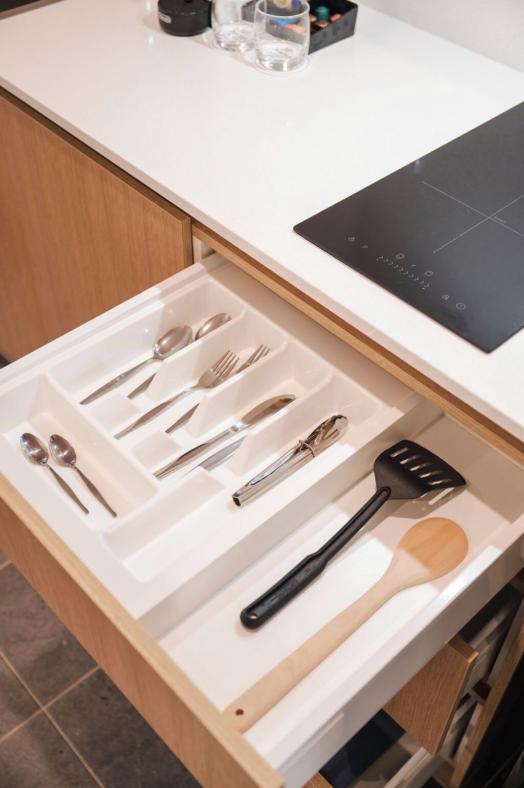 Un cajón de cocina con utensilios y una cocina por inducción negra.