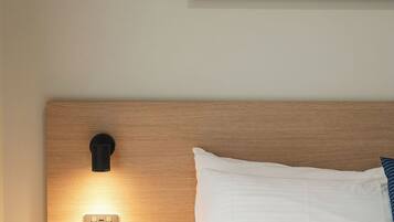 A bedroom with a wooden headboard, a bedside table with a lamp, a white bed, and a painting of a landscape.