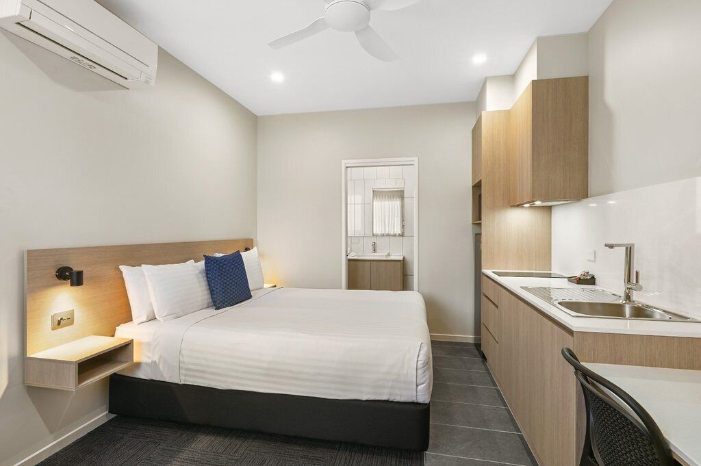 Una habitación de hotel moderna con cama, mesita de noche y una pequeña cocina.