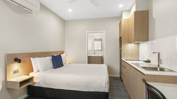 Una habitación de hotel moderna con cama, mesita de noche y una pequeña cocina.