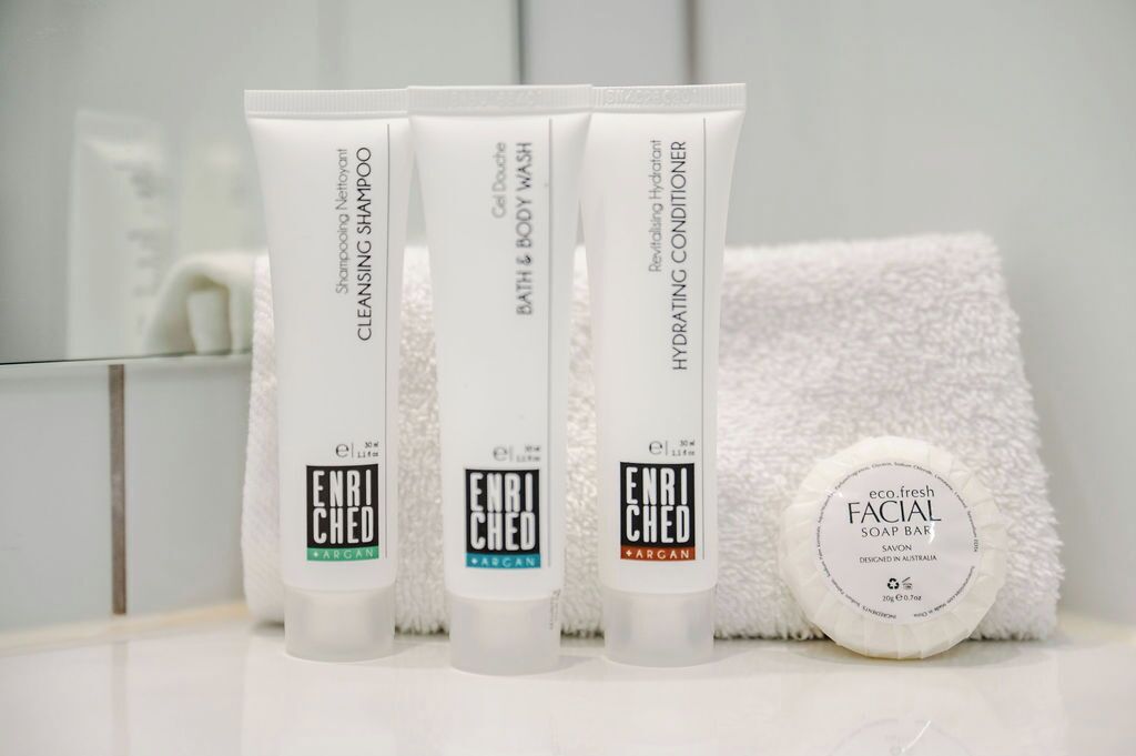 Tres productos para el cuidado de la piel y una pastilla de jabón facial sobre una encimera de baño.