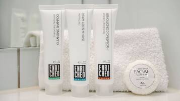 Tres productos para el cuidado de la piel y una pastilla de jabón facial sobre una encimera de baño.