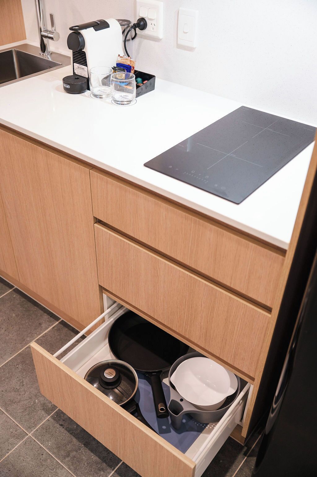 A kitchen with a white countertop, a black induction cooktop, and a drawer with cooking utensils.