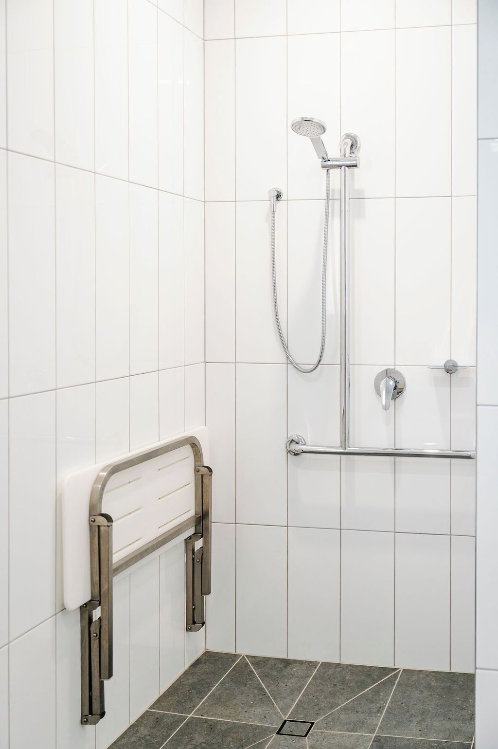 A shower area with white tiled walls, a grab bar, and a showerhead.