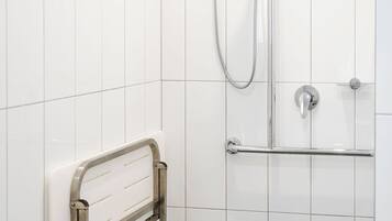 A shower area with white tiled walls, a grab bar, and a showerhead.