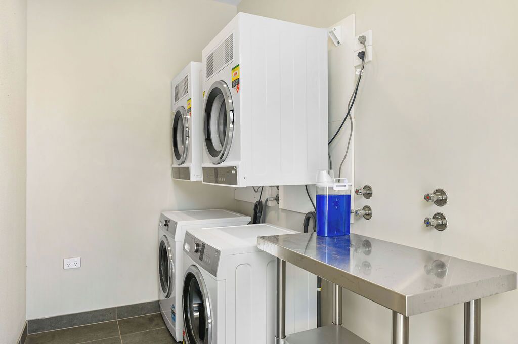 Un espace buanderie équipé de deux machines à laver et d’un sèche-linge, d’une table en acier inoxydable et d’un bac bleu.