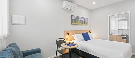Habitación de hotel con cama, escritorio con silla, sofá, equipo de aire acondicionado, un cuadro en la pared y ventana con cortinas.