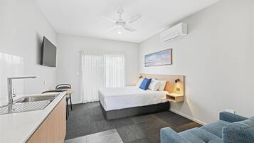 Habitación de hotel moderna con cama, escritorio con silla, televisor, ventilador de techo y ventana con cortinas.