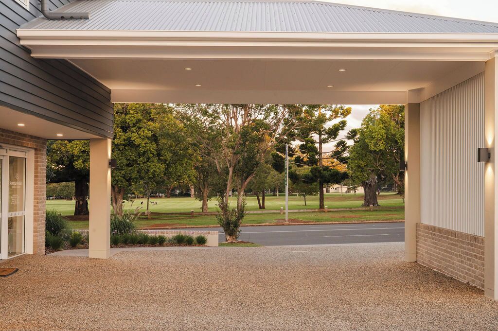 A covered outdoor area with a gravel driveway, trees, and a grassy lawn.