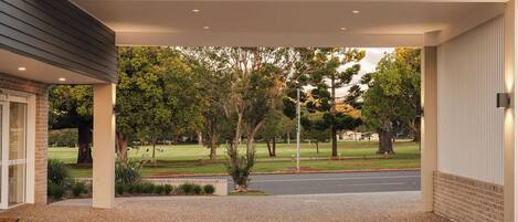 A covered outdoor area with a gravel driveway, trees, and a grassy lawn.
