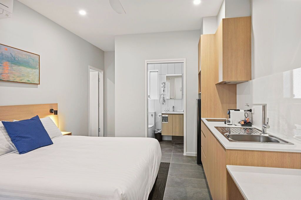 Una habitación de hotel con cama, una kitchenette pequeña, un baño y un cuadro en la pared.