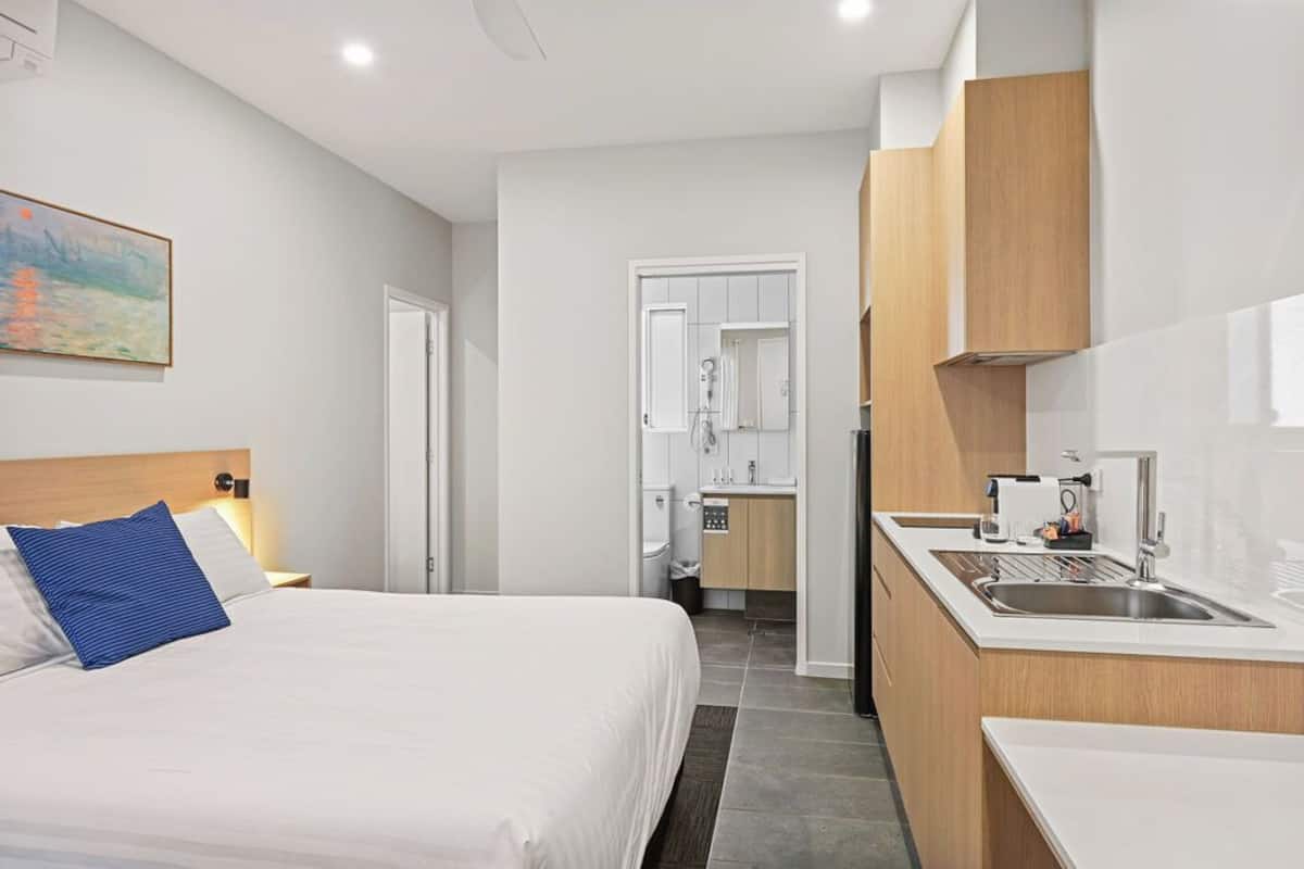 Una habitación de hotel con cama, una kitchenette pequeña, un baño y un cuadro en la pared.