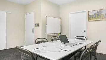 A conference room with a white table, four chairs, a laptop, and a whiteboard.