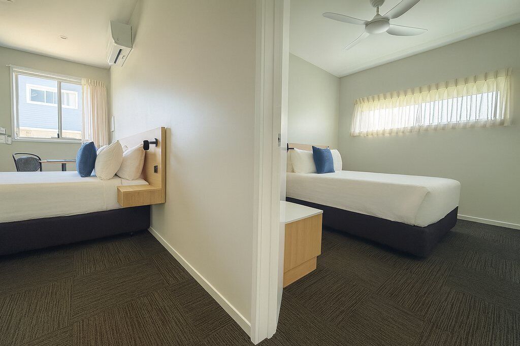 Habitación de hotel con dos camas, ventilador de techo y ventana con cortinas.