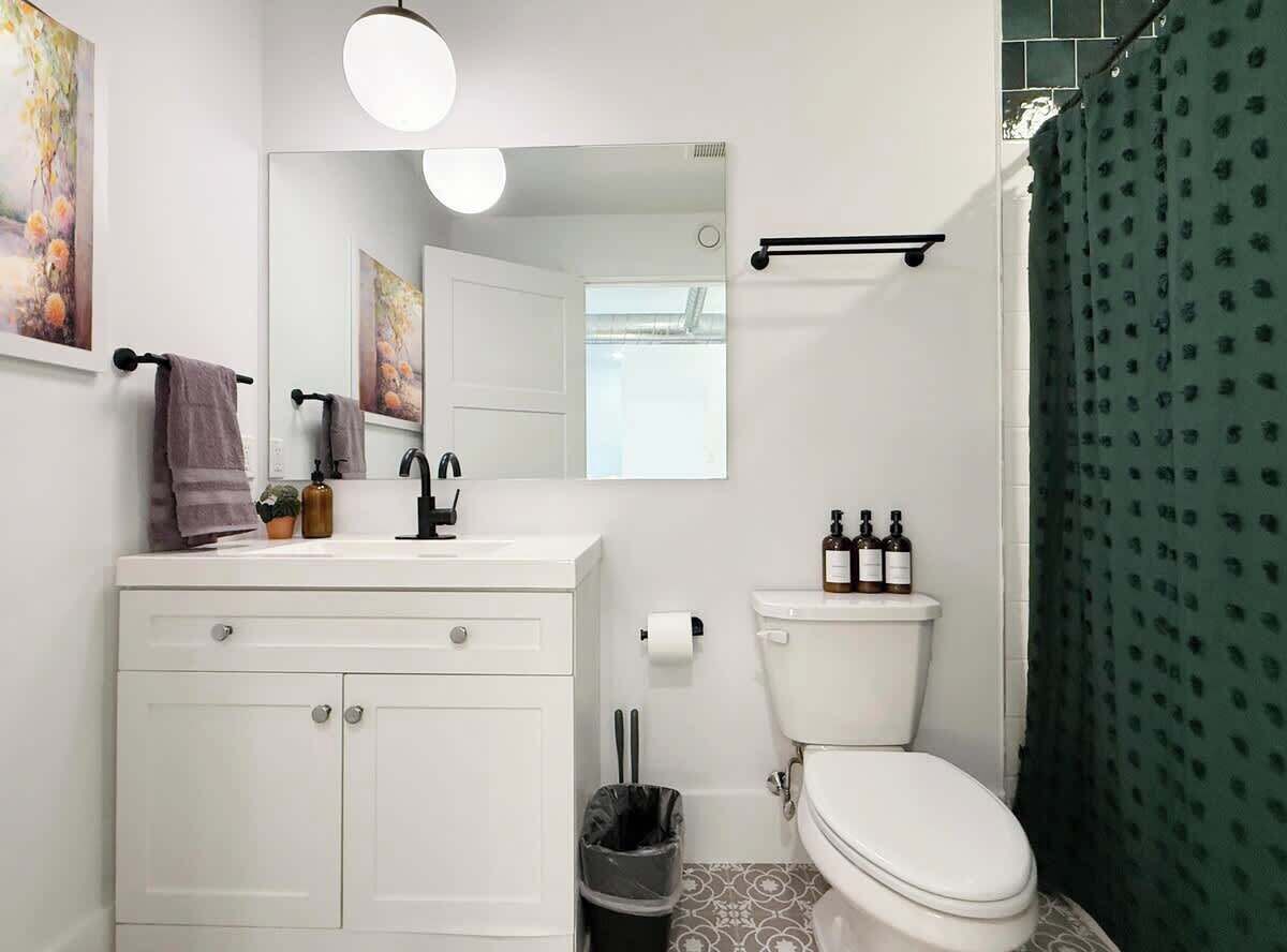 Un baño con lavabo blanco, espejo, inodoro y cortina de ducha verde.