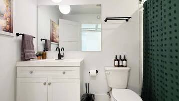 Un baño con lavabo blanco, espejo, inodoro y cortina de ducha verde.