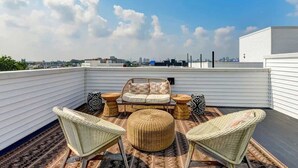 Une terrasse sur le toit, aménagée avec des meubles en osier, un pouf rond et offrant une vue panoramique sur la ville.