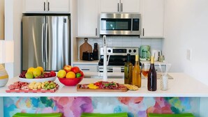 Une cuisine moderne dotée d’appareils électroménagers en acier inoxydable, d’un tableau abstrait aux couleurs vives et d’un coin bar avec des tabourets.