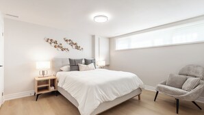 Quarto moderno com cama grande, mesas de cabeceira com luminárias, um painel decorativo na parede e uma janela com persianas.