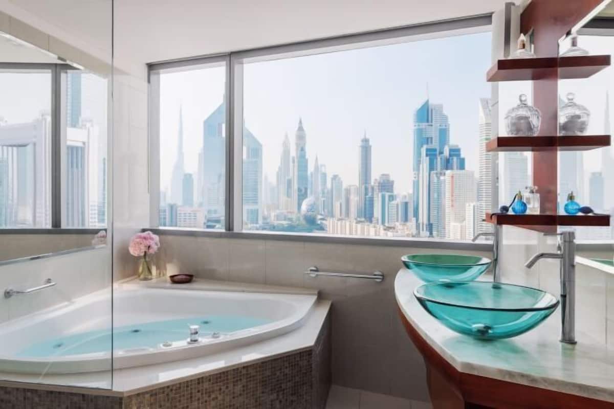 A modern bathroom with a glass-enclosed bathtub, a vanity with a glass bowl sink, and a view of a city skyline.