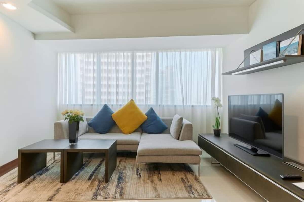 A modern living room with a sofa, coffee table, TV, and a large window with sheer curtains.