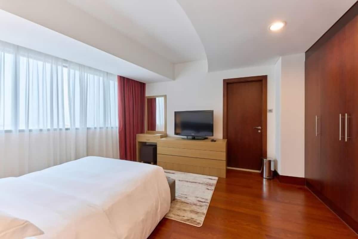 A hotel room with a bed, a TV on a wooden dresser, a wardrobe, and a window with curtains.