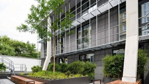 A modern building with a glass facade, outdoor seating, and greenery.