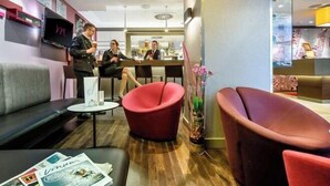 A modern hotel lobby with red seating, a reception desk, and a bar area.
