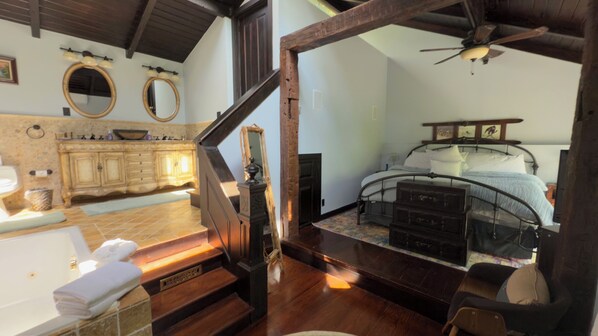 Un dormitorio con cama, una escalera de madera, un baño con lavamanos y espejo, y vistas al exterior.