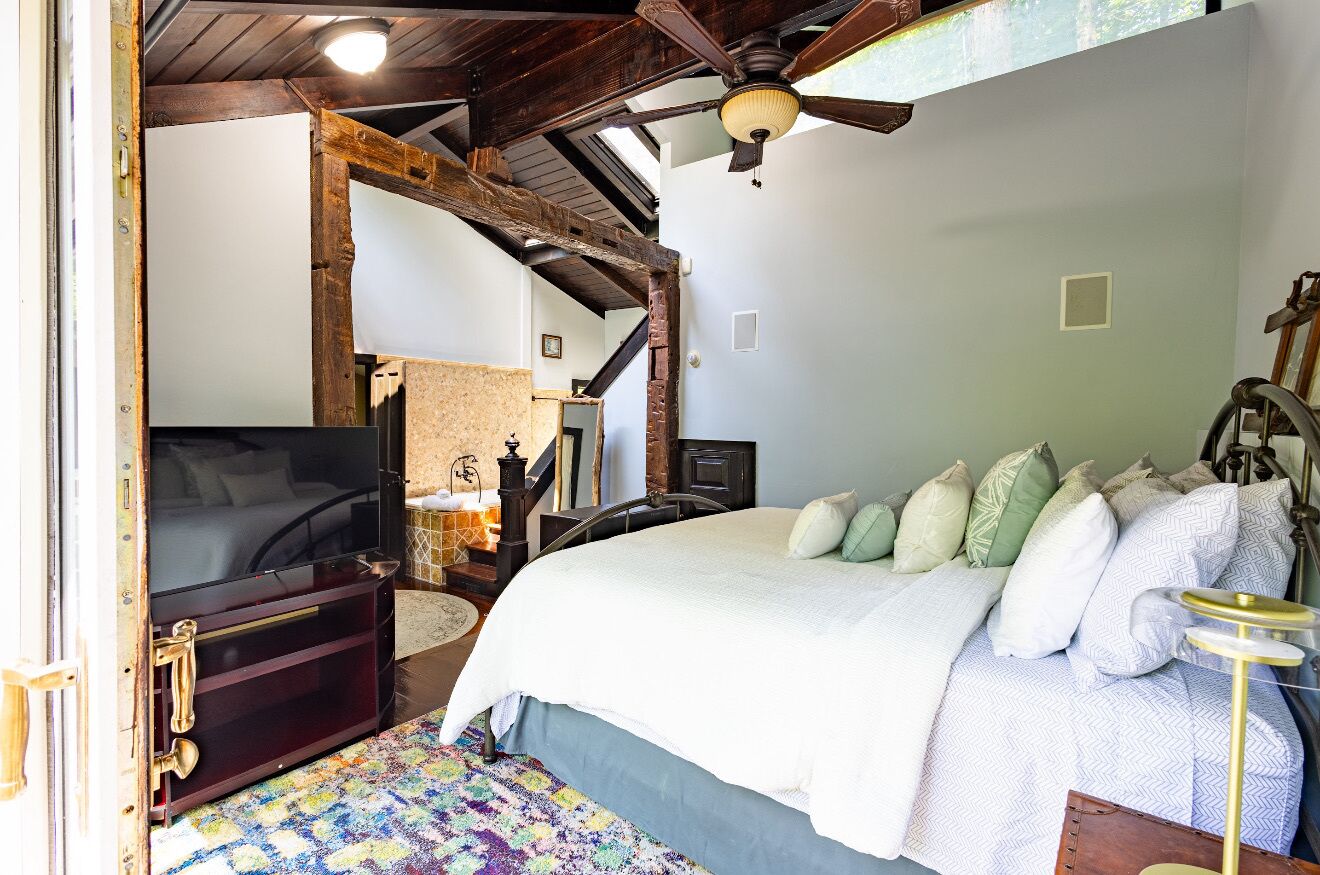 A bedroom with a large bed, a ceiling fan, a television, and a rustic wooden ceiling.