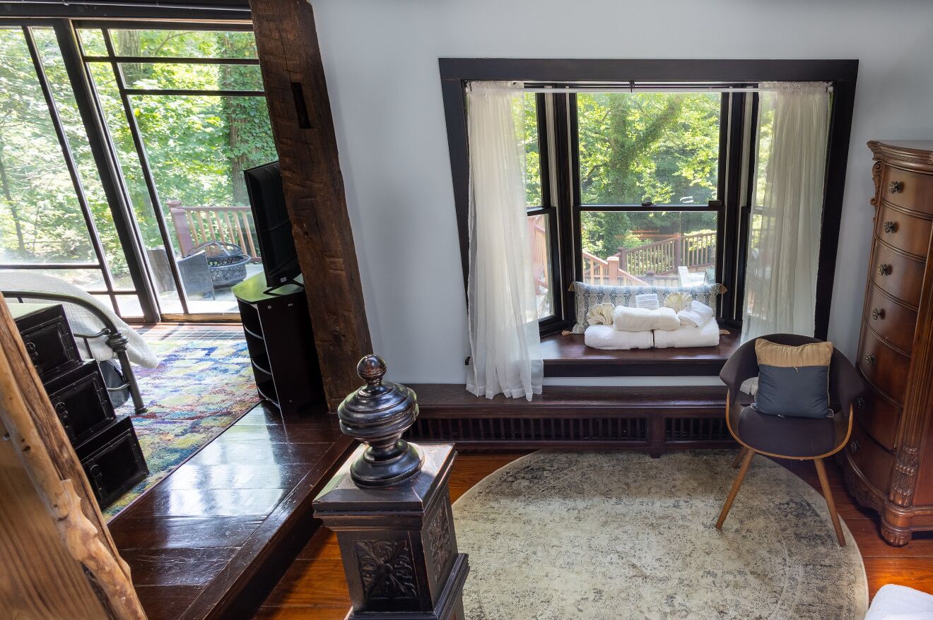 Una habitación con un ventanal grande, una silla de madera, un aparador y una alfombra.