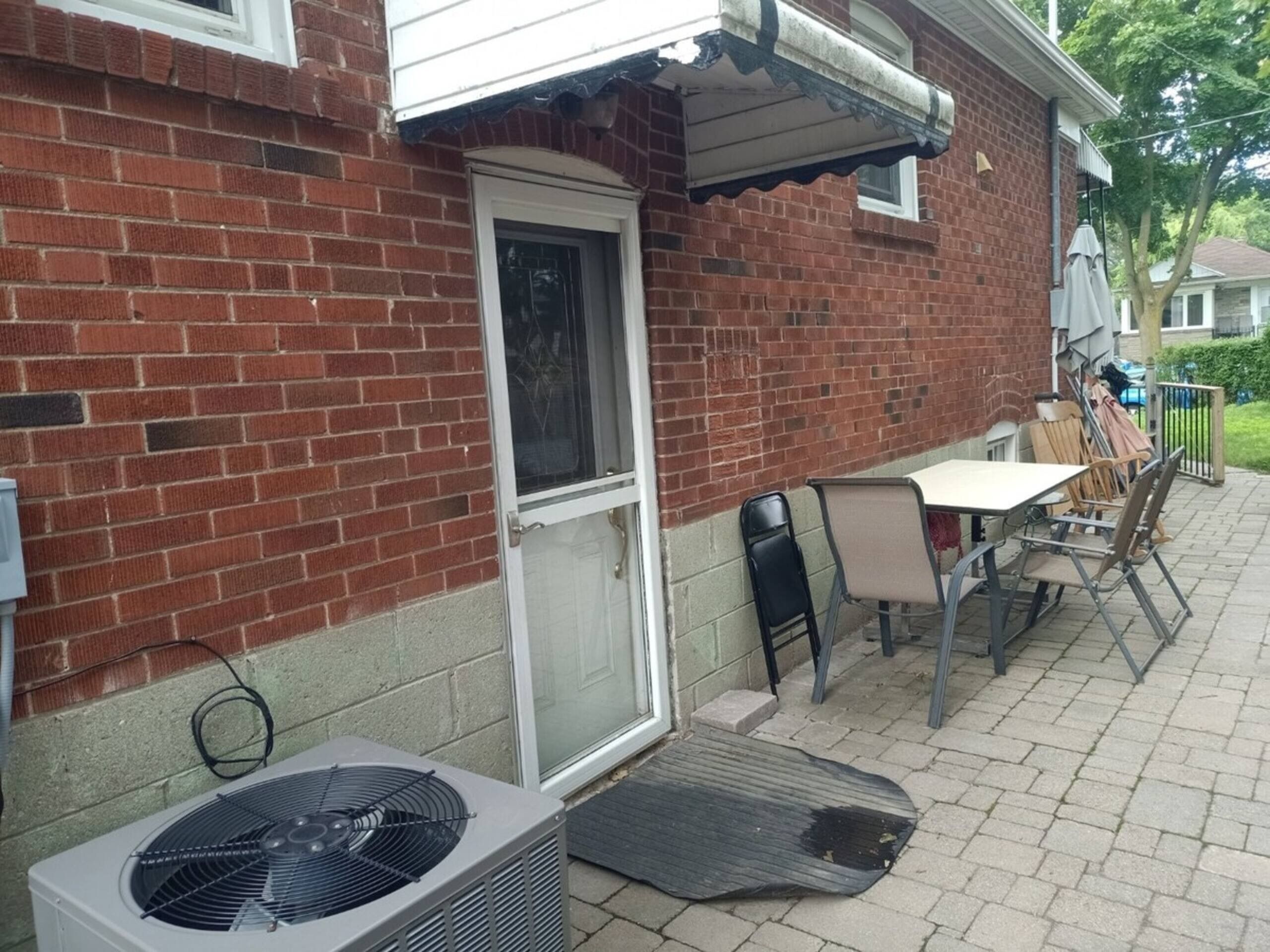 A brick house with a door, a small patio with a table and chairs, and an air conditioning unit.