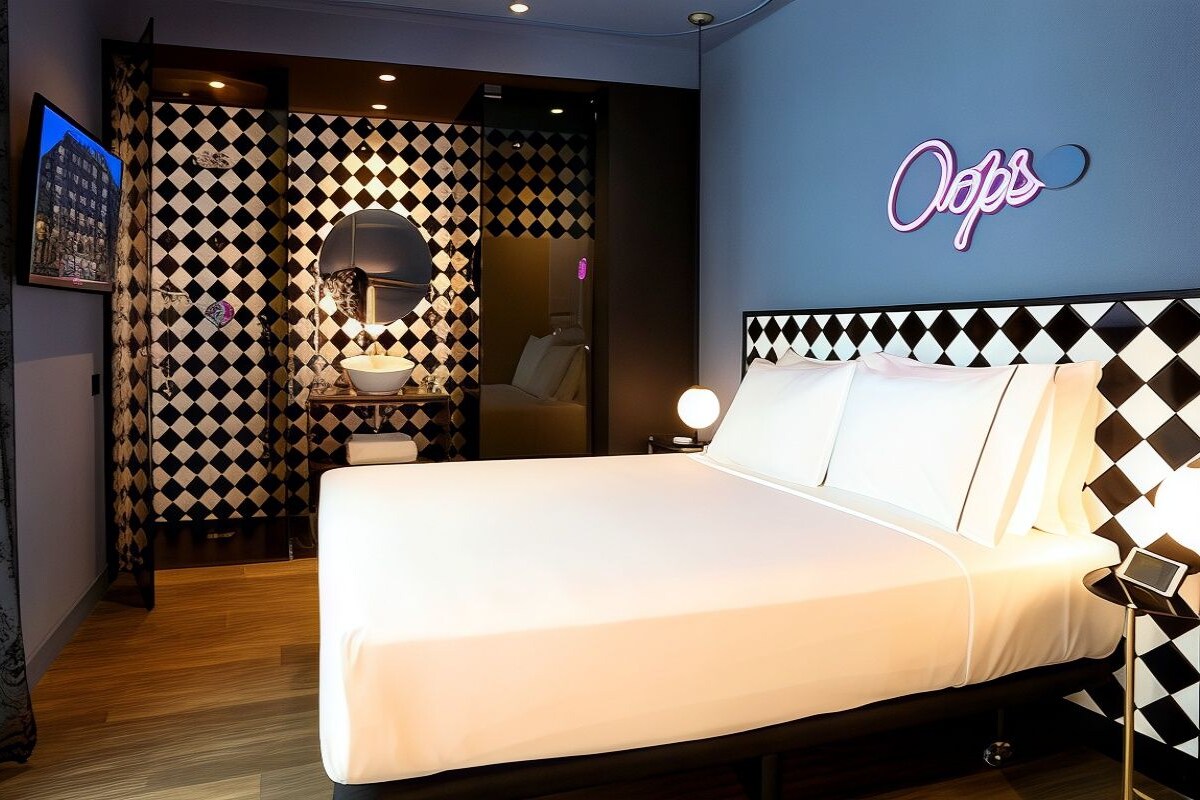 Ein Hotelzimmer mit einem Bett, einem Nachttisch, einem Spiegel und einer Wand mit einem Neonzeichen.