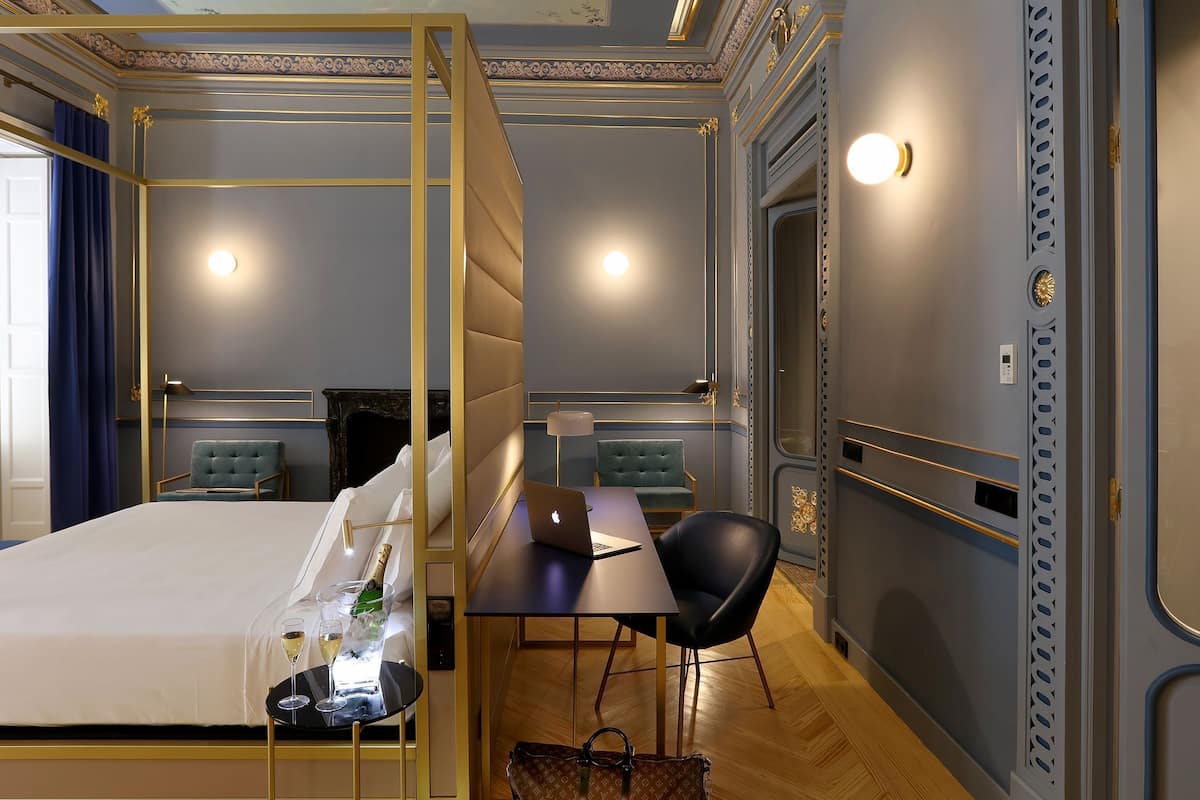 A bedroom with a bed, bedside table, lamp, chair, and a view of a bathroom through a door.